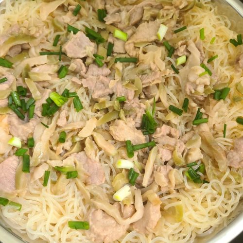 Steamed rice noodles with pork and pickled mustard on a white plate topped with scallions
