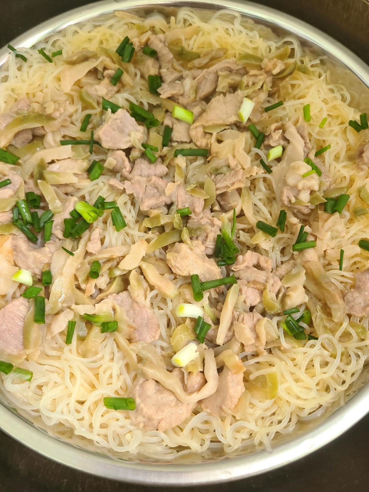Steamed rice noodles with pork and pickled mustard on a white plate topped with scallions