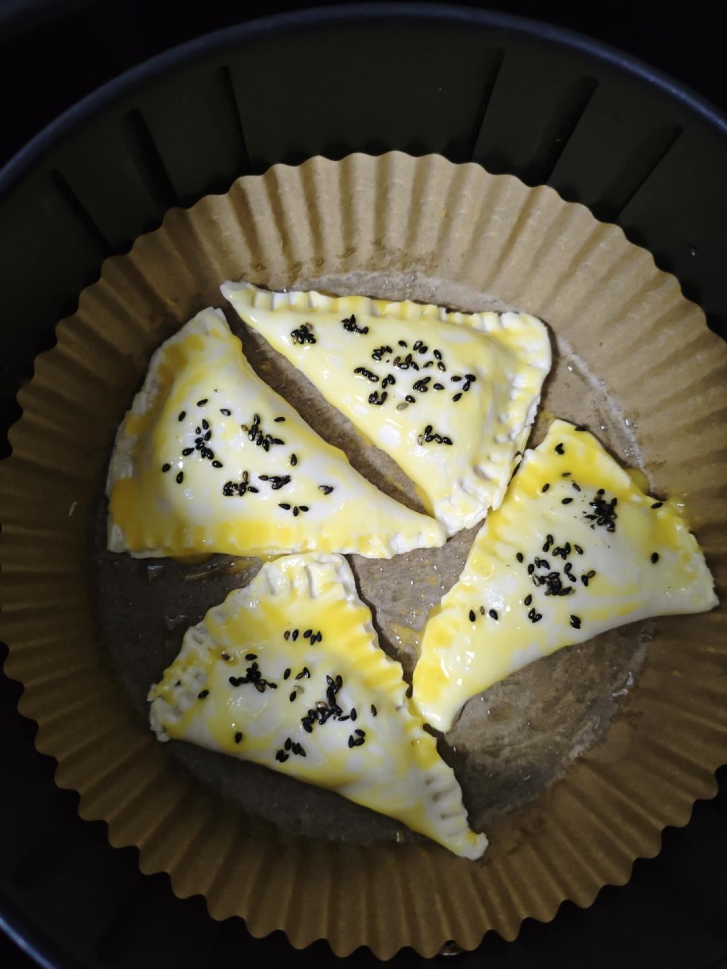 Grease the parchment paper with oil, set the pie parcels on it, brush them with the egg yolk wash, and scatter on a few black sesame seeds.