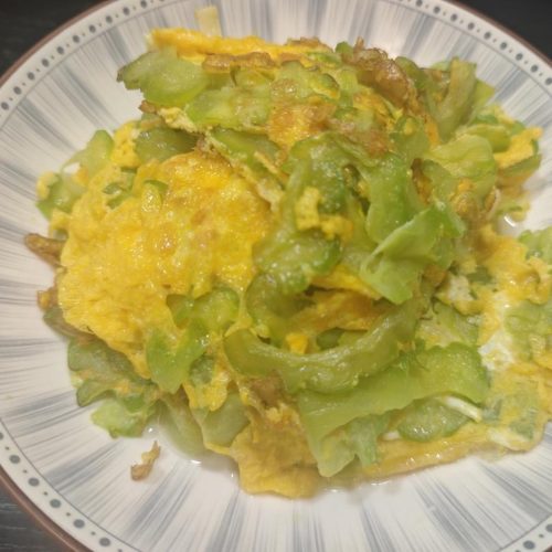 Bitter melon omelette in a wok, golden egg set over translucent slices of bitter gourd