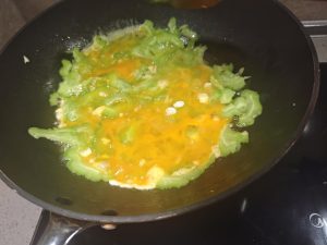 Drizzle a little more oil around the edge of the wok, pour the beaten egg evenly over the bitter melon, and tilt the wok so the egg settles into an even layer.