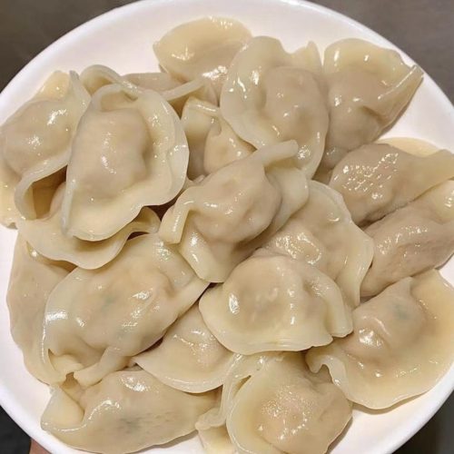 A plate of boiled frozen dumplings with a bowl of garlic chili dipping sauce