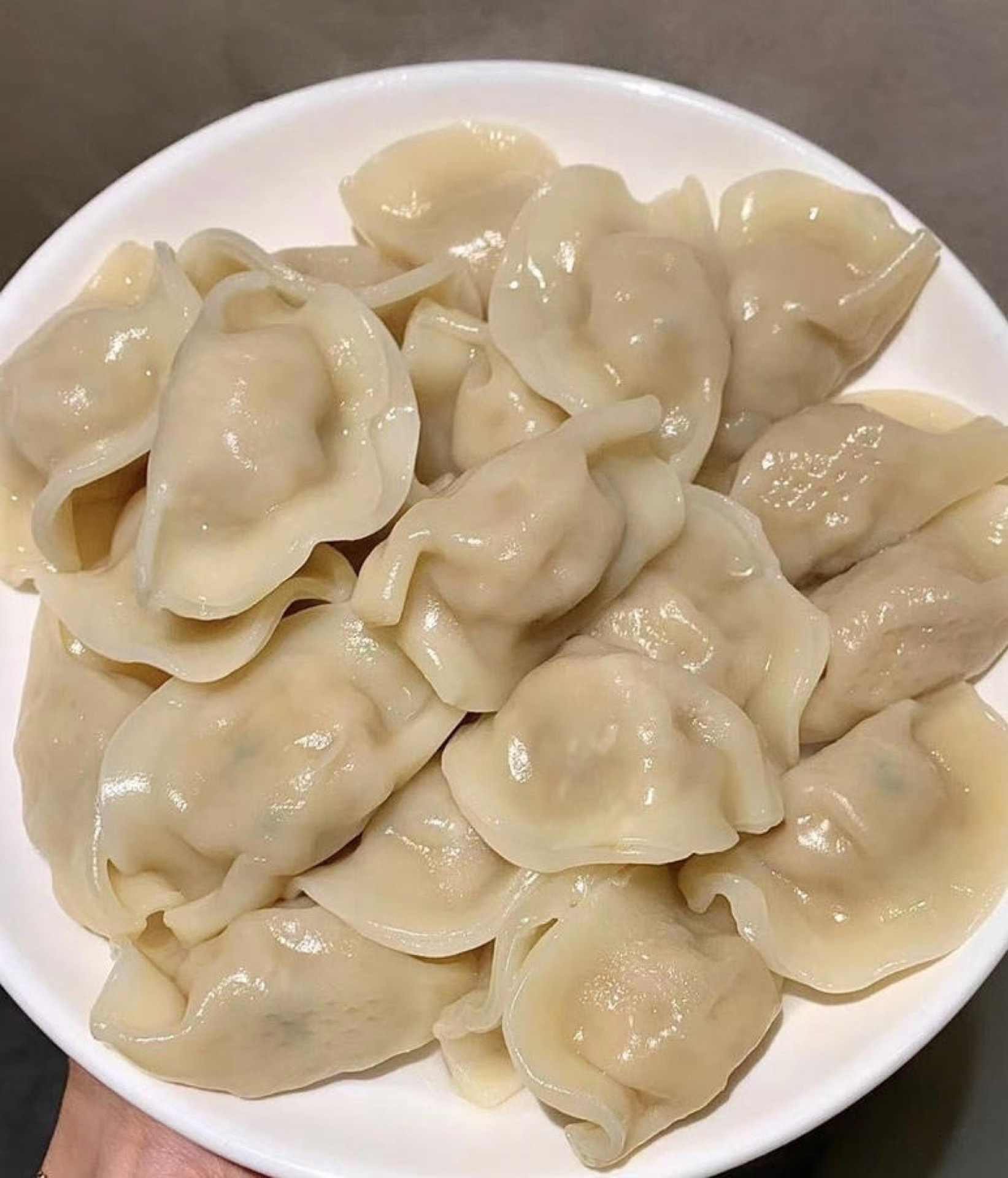 A plate of boiled frozen dumplings with a bowl of garlic chili dipping sauce