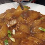 Braised daikon with minced pork served in a white bowl, glossy radish chunks topped with green scallions