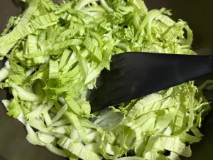 Heat the wok over medium heat, add the oil and the two star anise, then add the cabbage, pour in a small bowl of pork bone broth, sprinkle in some salt, cover with a lid, and let i