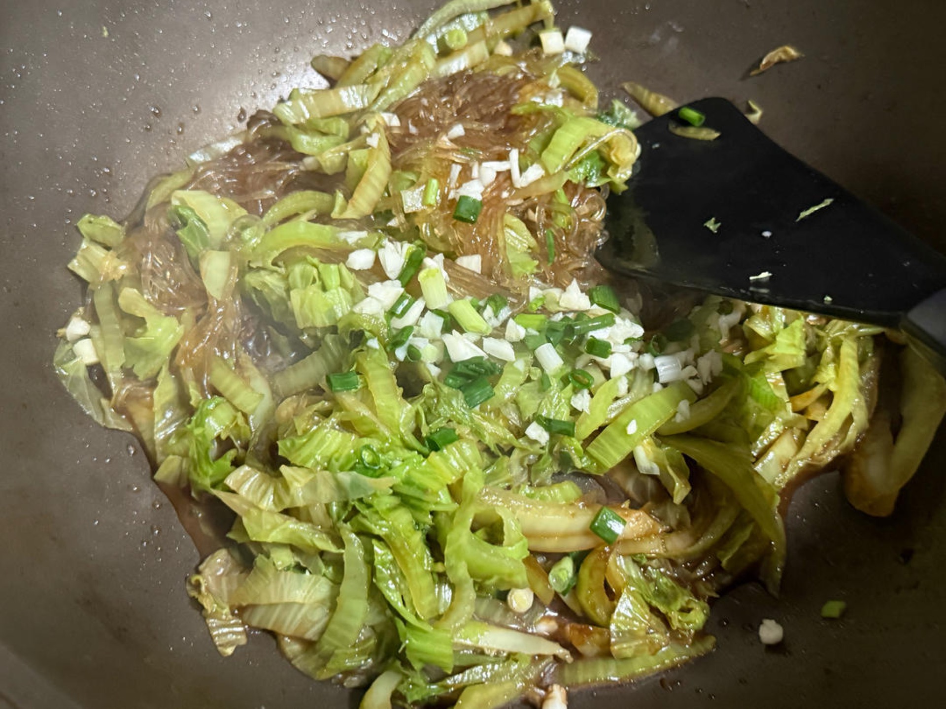 Add the soaked vermicelli to the wok and scatter the chopped scallions and minced garlic over the top.