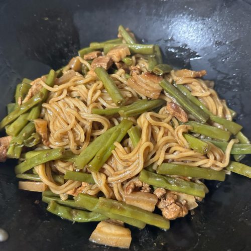 Braised noodles with green beans and pork belly in a wok