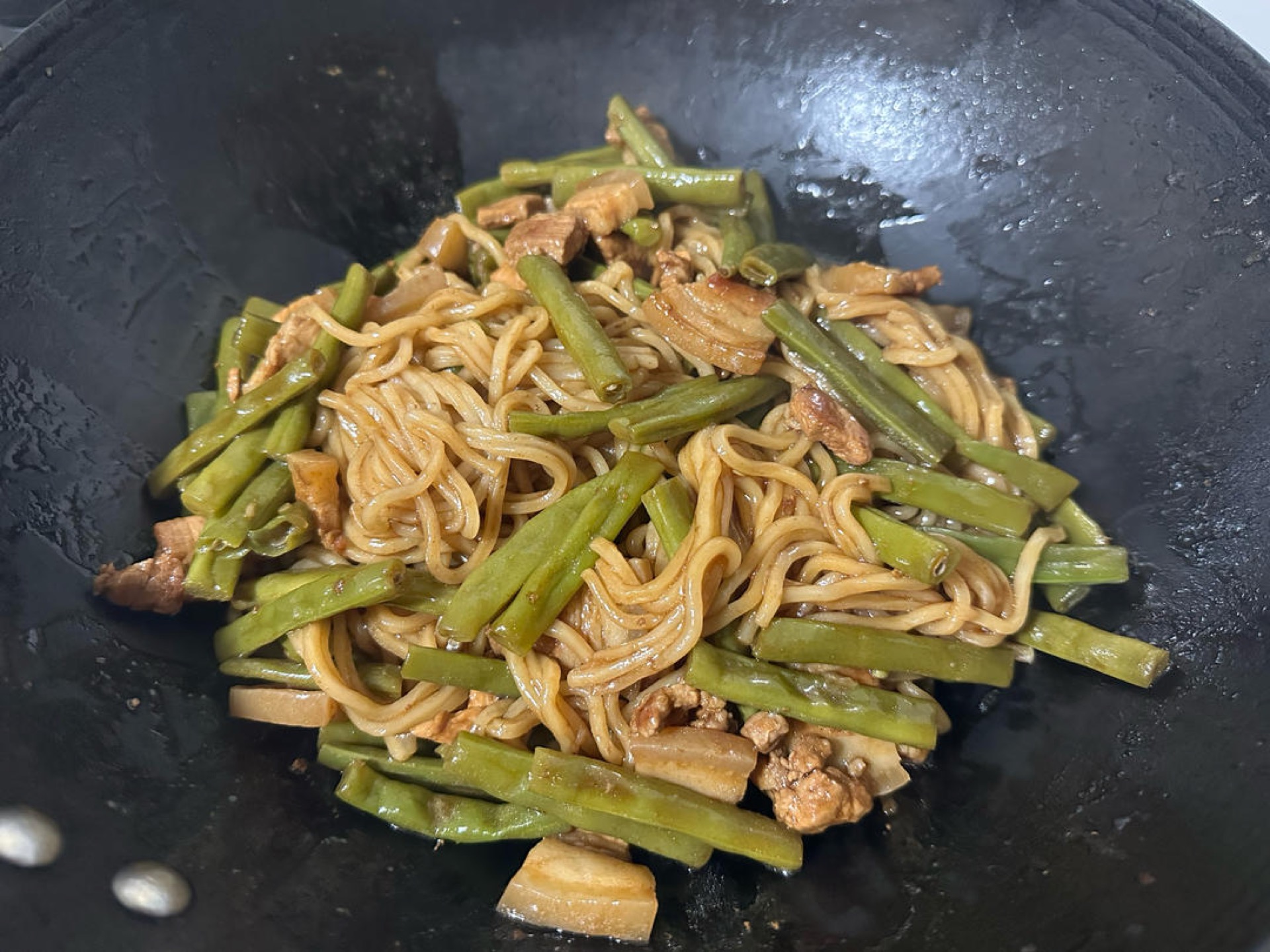 Braised noodles with green beans and pork belly in a wok
