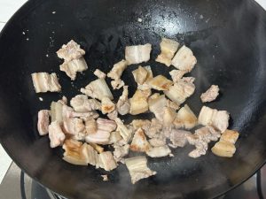 Heat a splash of oil in a wok over medium heat, add the sliced pork belly, and fry until the fat renders out and the edges are lightly browned and dry.
