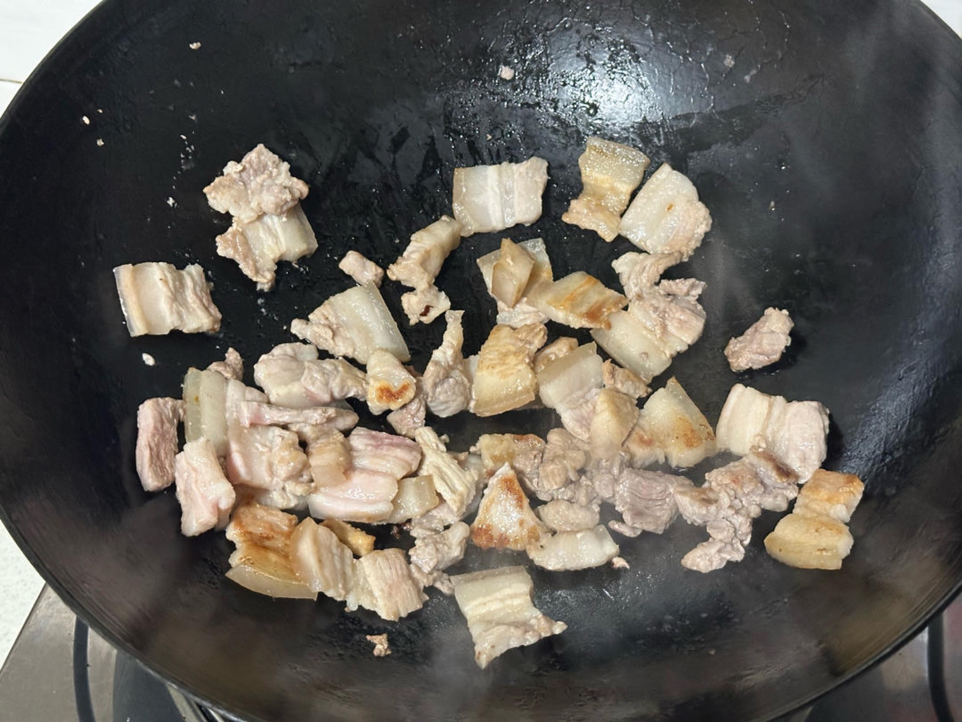 Heat a splash of oil in a wok over medium heat, add the sliced pork belly, and fry until the fat renders out and the edges are lightly browned and dry.
