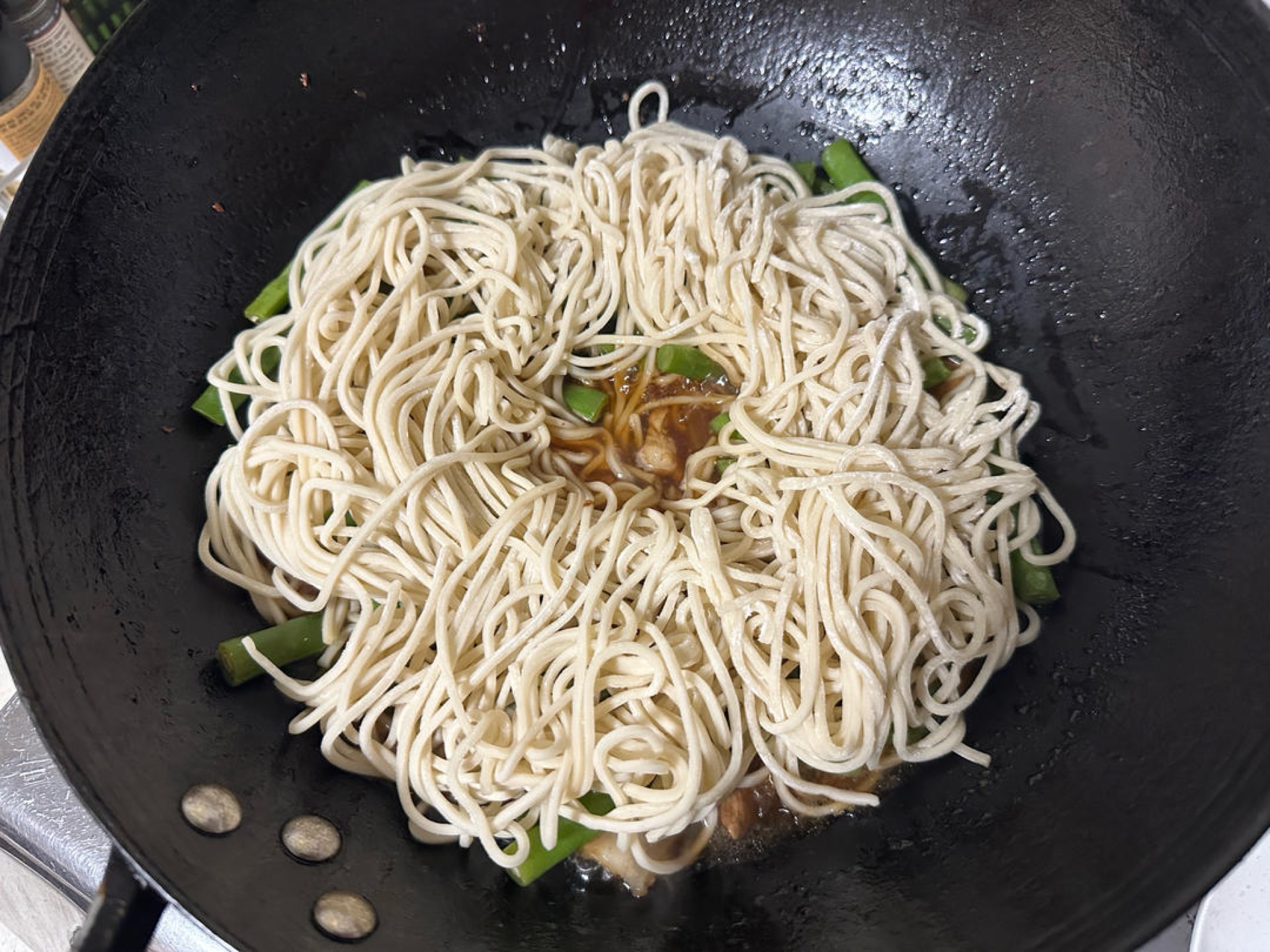 Loosen the noodles and spread them over the top, keeping them away from the sides of the wok, poke a hole through the center for steam to escape, cover, and steam over medium heat