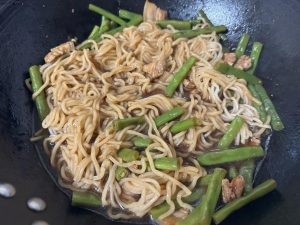 Lift the lid, flip the noodles over, pour the reserved half bowl of broth back in so the top noodles soak it up, and steam for another 5 minutes, checking often so nothing burns; w