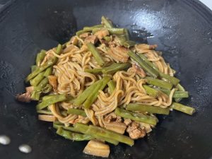 Uncover, toss the noodles with the beans and pork, and serve hot straight from the wok.