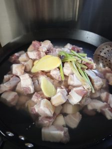 Add cold water, scallion, ginger and Shaoxing wine, bring to a rolling boil over high heat and cook for 2 to 3 minutes, then scoop the pork out, rinse away the scum under warm wate