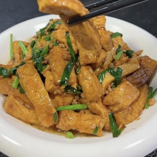 Braised tofu with chives served on a white plate with glossy sauce