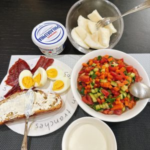A glass of milk, two eggs, a smear of cream cheese, stacked with egg, a few bites of vegetable salad, and a sprinkle of small dried meat.