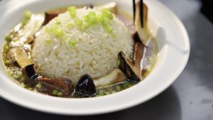 Steaming hot rice, a scattering of cilantro, a ladle of chicken broth over the top, and the fried mushrooms arranged on it — that's a bowl of chicken soup rice that comforts the he