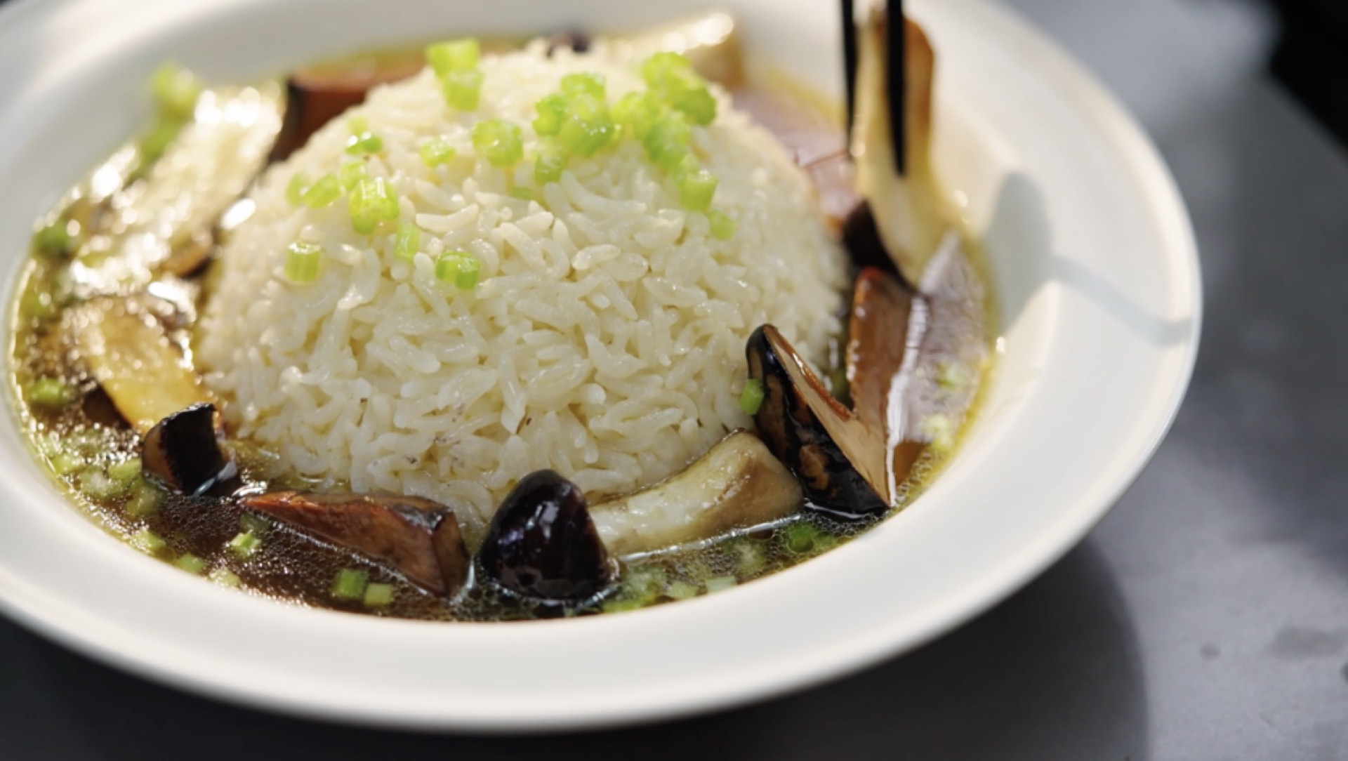 Steaming hot rice, a scattering of cilantro, a ladle of chicken broth over the top, and the fried mushrooms arranged on it — that's a bowl of chicken soup rice that comforts the he