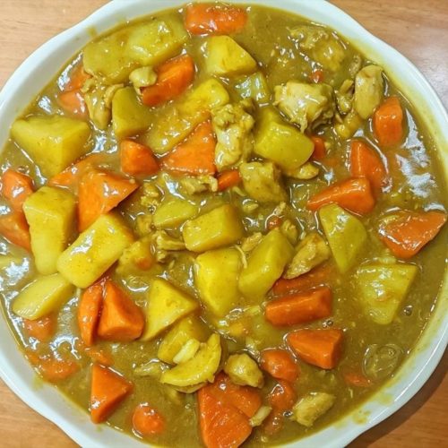 Curry chicken with potato and carrot served in a white bowl, glossy curry gravy over tender chicken chunks and vegetables