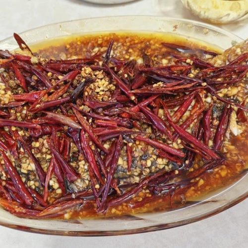 Garlic blast fish on a white plate topped with garlic sauce and sizzling chili oil