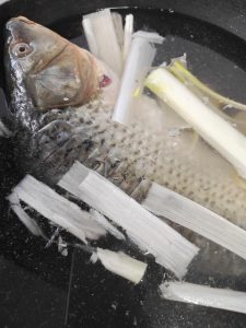 Clean the fish well, score the back with a few shallow cuts, and lower it into a pot of cold water with smashed scallion whites, ginger, Shaoxing wine, and white pepper; once the w