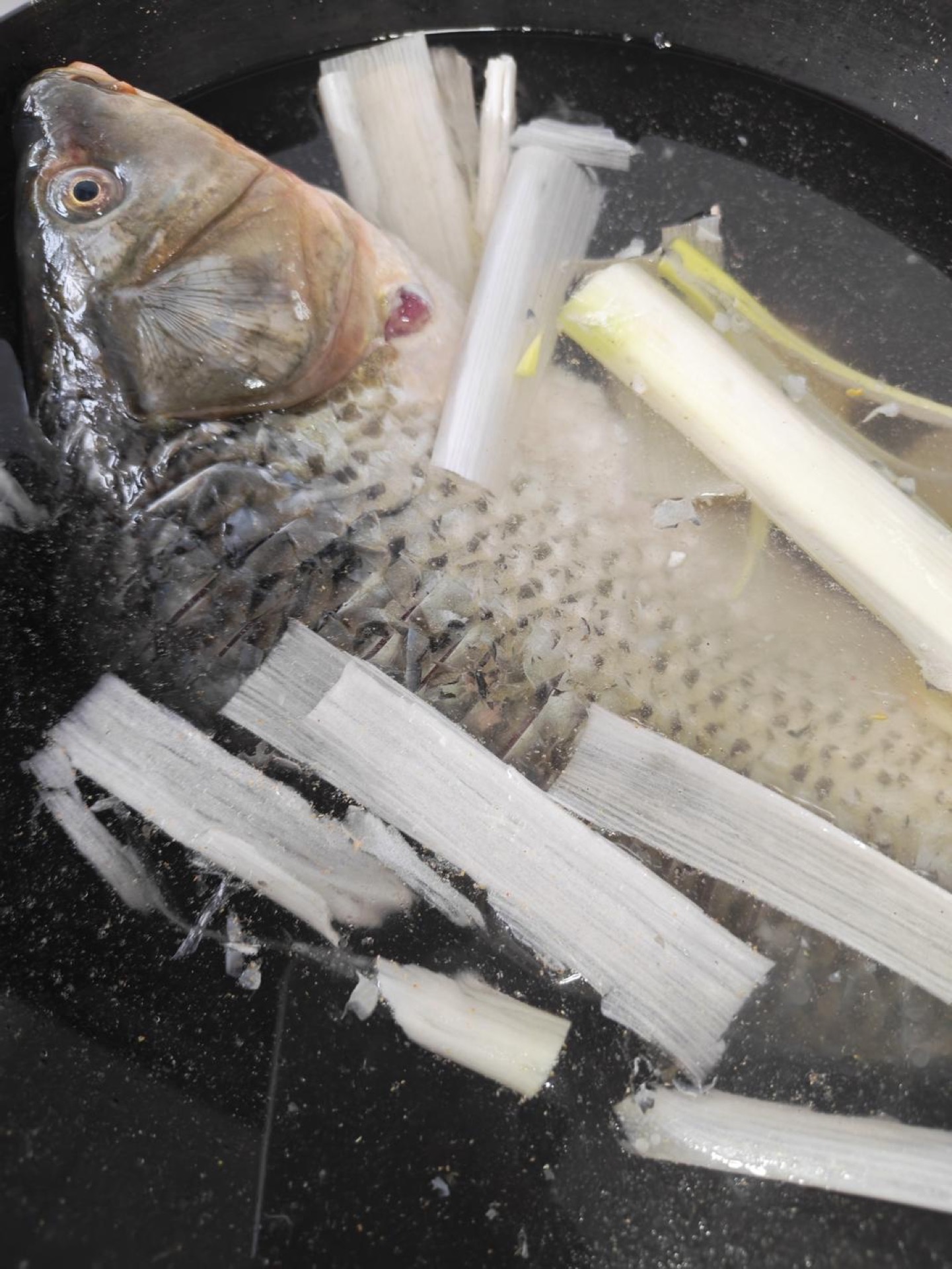 Clean the fish well, score the back with a few shallow cuts, and lower it into a pot of cold water with smashed scallion whites, ginger, Shaoxing wine, and white pepper; once the w