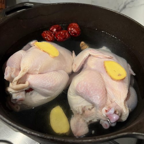 Ginseng chicken soup in a pot with a whole stuffed chicken, jujubes and scallions