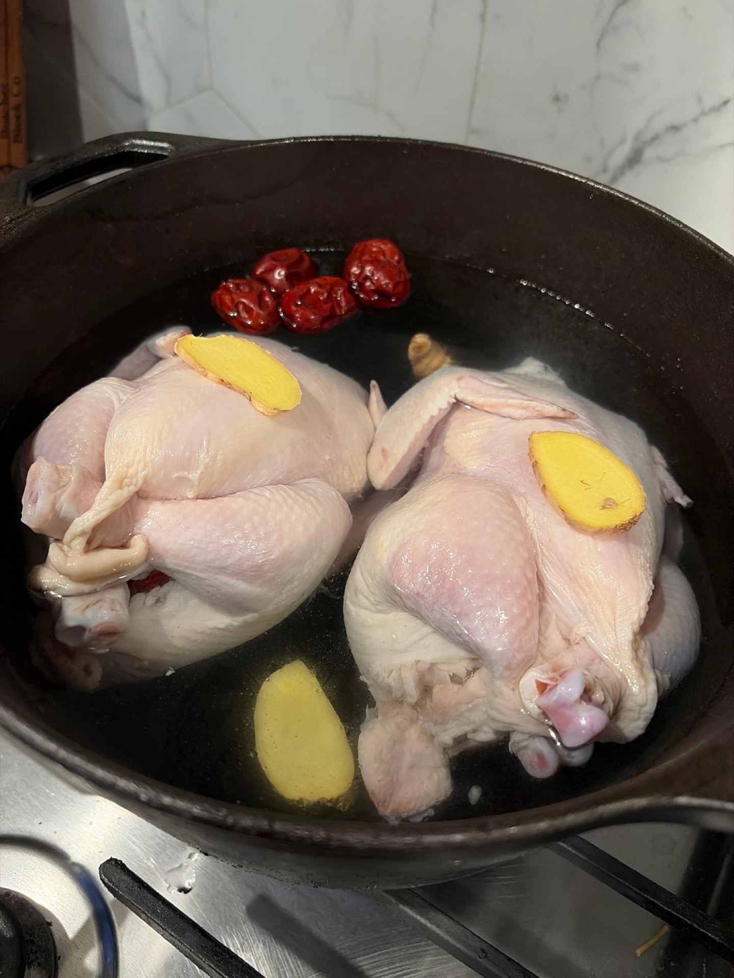 Ginseng chicken soup in a pot with a whole stuffed chicken, jujubes and scallions