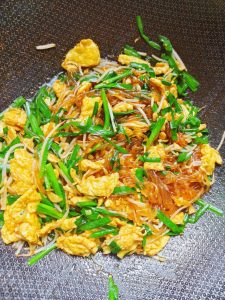 Add the dressed sweet potato noodles, the scrambled eggs, and the chives to the wok.