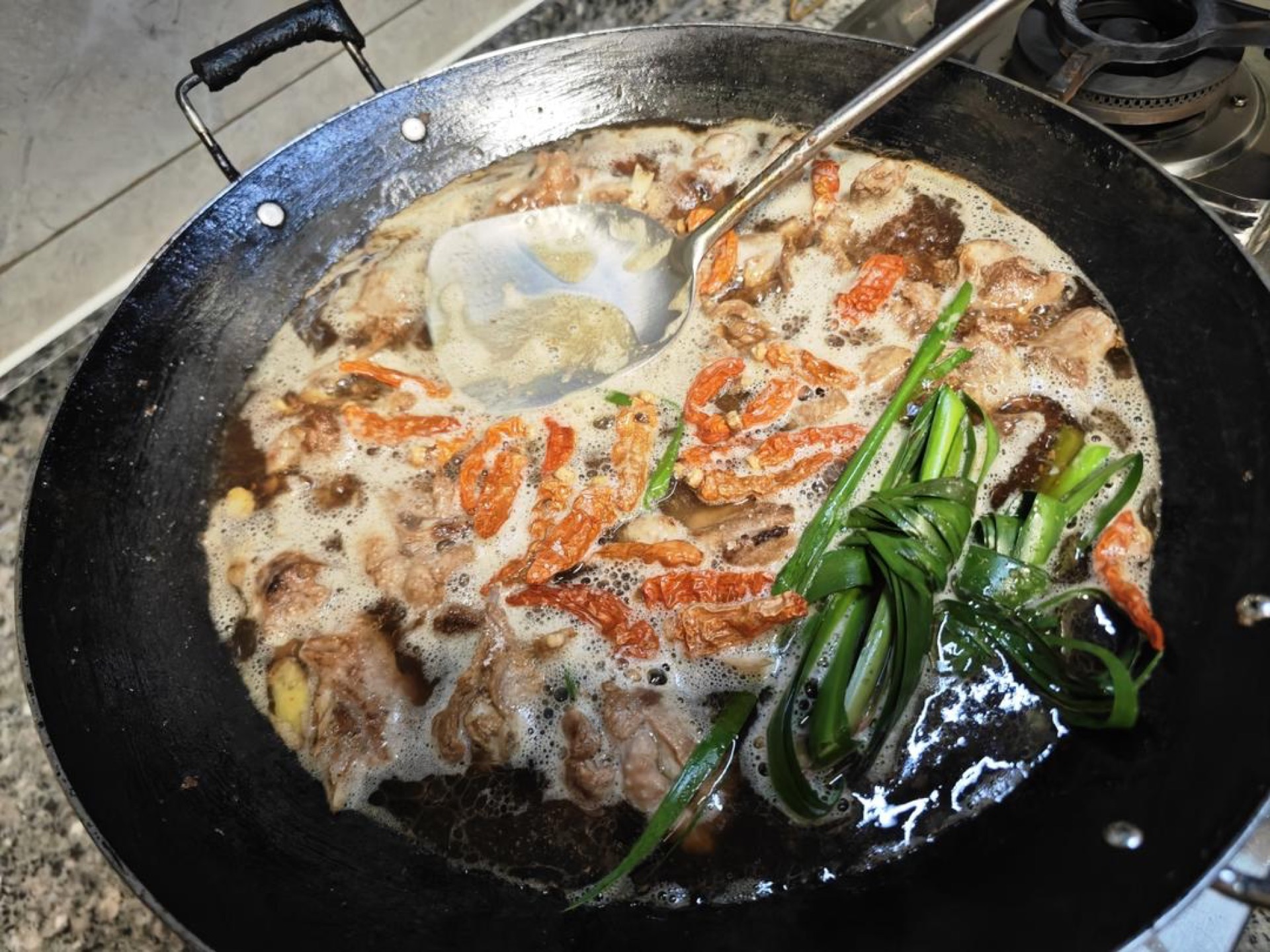 Pour in the bottle of beer, or 2/3 cup of rice wine if you have it — rice wine braises more fragrantly, but beer works if not — add the dried chilies and lemongrass, and simmer for