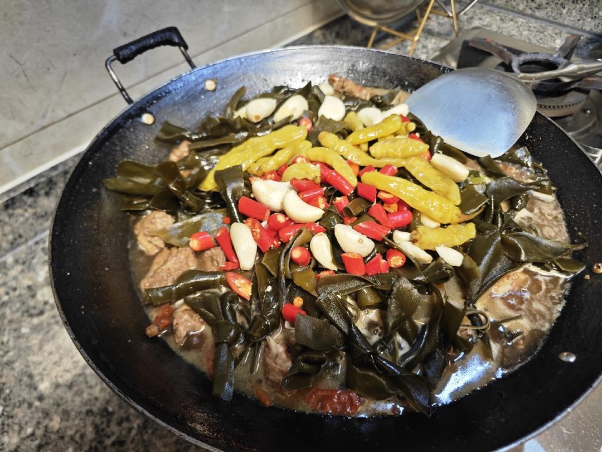 Add the kelp, garlic, small chili peppers, and pickled chilies, cover, and simmer for 20 minutes without stirring them in evenly — just lay them on the surface, cover, and let them