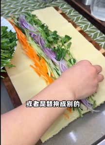 Julienne 1 carrot, 1/2 onion, and 1 cucumber into thin strips, and cut a small handful of cilantro into segments. Lay a whole sheet of tofu skin flat and arrange the vegetables in