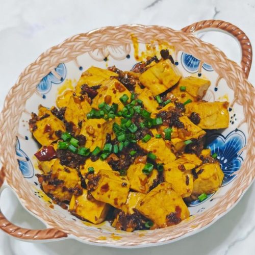 Mapo tofu with beef crisp in a dark bowl topped with scallions and red chili oil
