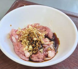 Slice the pork into thin shreds, add the minced scallion, light soy sauce, dark soy sauce, and Shaoxing wine, and stir well to marinate.