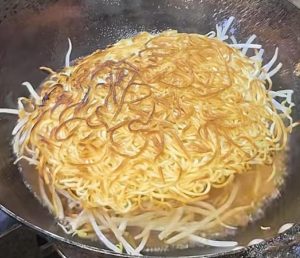 Add the bean sprouts to the gravy, lay the pan-fried noodles on top of the sprouts, cover the wok with a lid, and cook for 3 to 5 minutes.