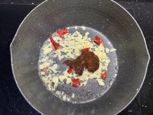 Without washing the wok, add a little oil, add the minced garlic and dried chilies and fry until fragrant, then add two spoonfuls of dry pot sauce and stir over low heat until arom