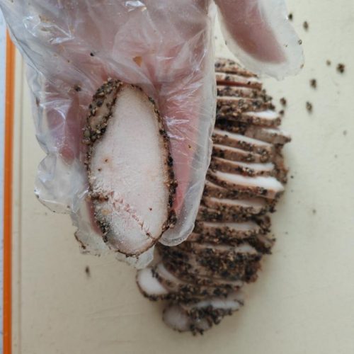 Sliced pastrami-style chicken breast fanned on a wooden board with cracked black pepper