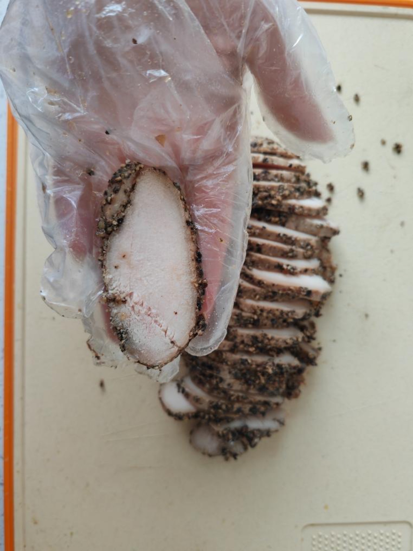 Sliced pastrami-style chicken breast fanned on a wooden board with cracked black pepper
