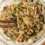 A bowl of quick fried sauce noodles topped with savory pork sauce, scallions, and chili