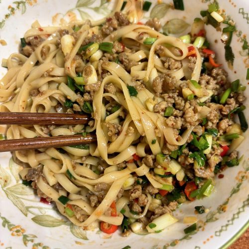 A bowl of quick fried sauce noodles topped with savory pork sauce, scallions, and chili
