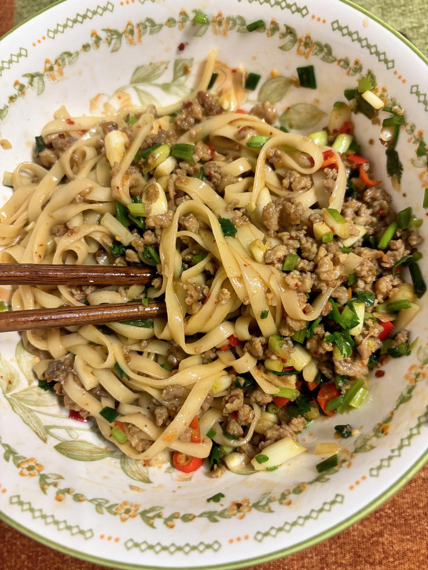 A bowl of quick fried sauce noodles topped with savory pork sauce, scallions, and chili