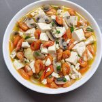 River shrimp and mushroom braised tofu in a shallow white dish, garnished with chopped scallions