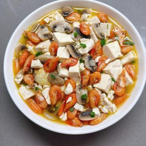 River shrimp and mushroom braised tofu in a shallow white dish, garnished with chopped scallions