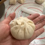 Scallion pork steamed buns on a bamboo steamer lined with parchment