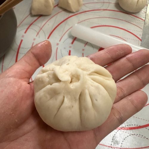 Scallion pork steamed buns on a bamboo steamer lined with parchment