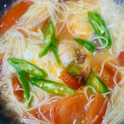 A bowl of shrimp tomato egg noodle soup with a fried egg, tomato wedges, and whole shrimp in a savory orange broth