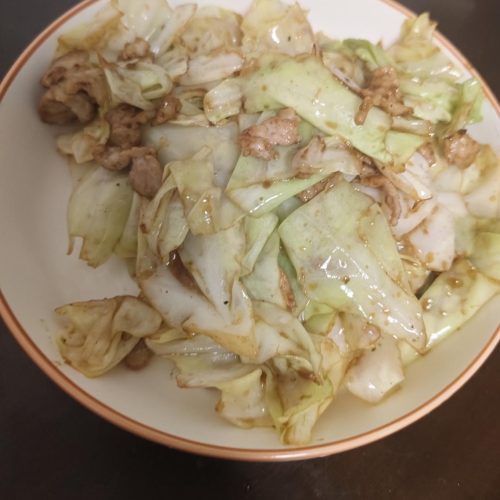 Stir-fried cabbage with pork served on a white plate with a side of steamed rice
