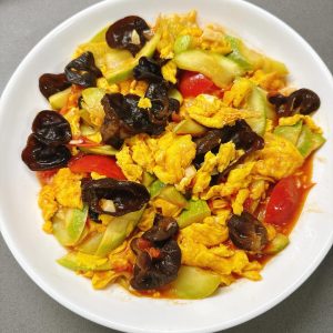 Stir-fried zucchini with eggs served in a white dish with silky scrambled eggs, crisp zucchini slices, wood ear mushrooms, and cherry tomatoes