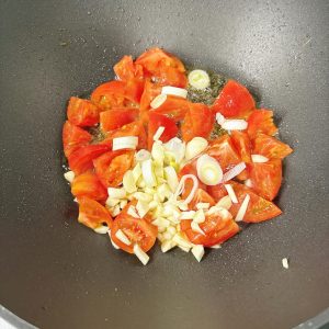 Leave the base oil in the wok, add the scallion and garlic and stir until fragrant, then add the tomato chunks.