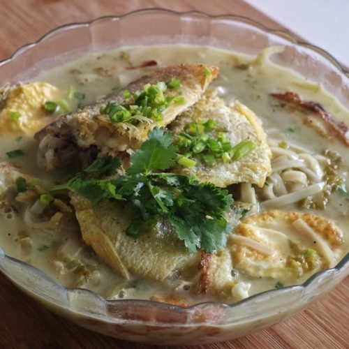 A bowl of pickled cabbage yellow croaker noodles with golden fried fish, fried egg, scallion and cilantro in milky broth